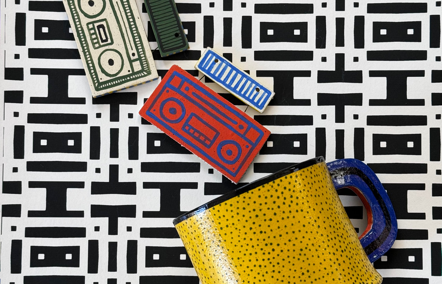 colorful ceramic boombox medallions spilling out of a yellow polka dot mug on top of a black and white pattern background that looks like cassette tapes